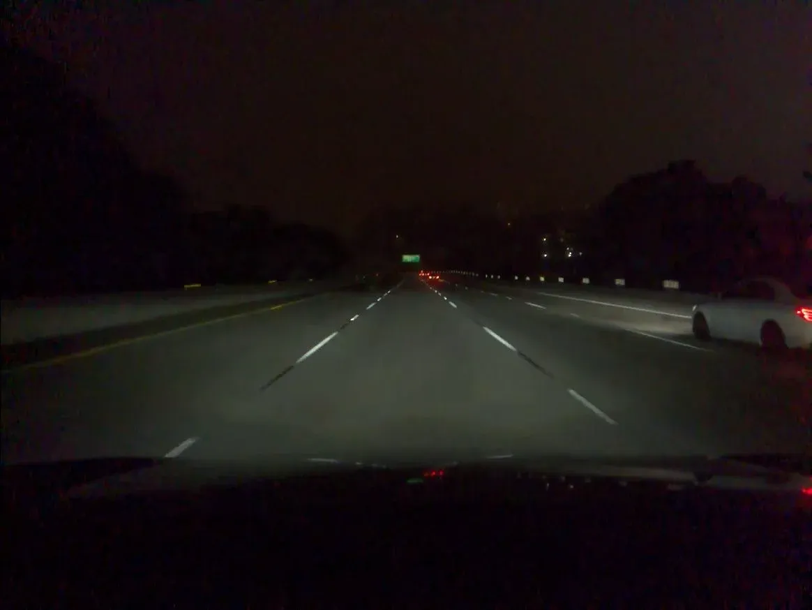 Nighttime highway scene with a white car near the right edge
