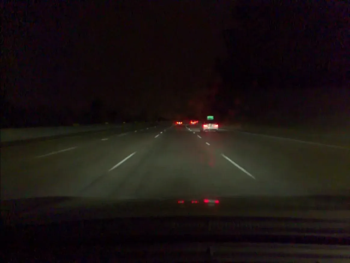 Nighttime highway scene approaching several cars