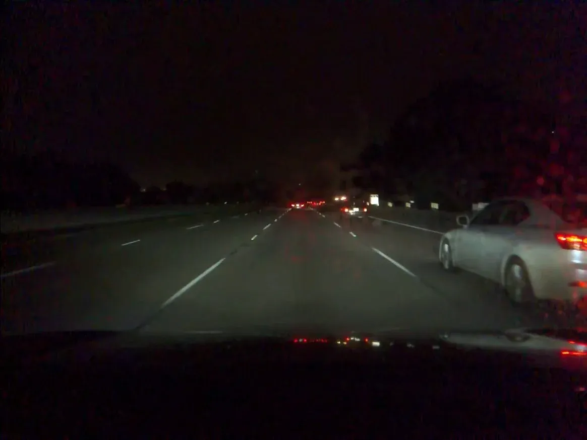 Nighttime highway scene with a silver car passing close on the right